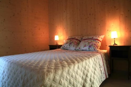 Cozy bedroom at Maison Addama with quilted bed, floral pillows, warm bedside lighting, and patterned wallpaper in Neyron