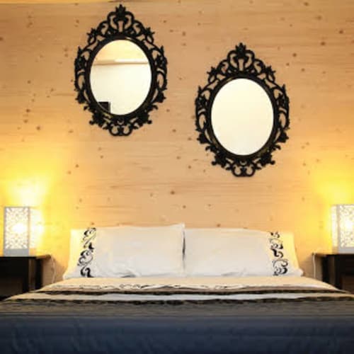 Dormitorio de la Maison Addama B&B en Neyron con espejos negros ornamentados sobre la cama e iluminación amarilla cálida