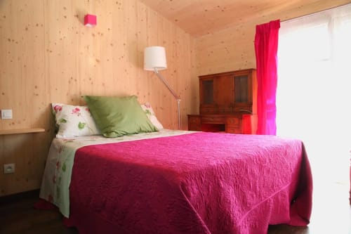 Habitación en Maison Addama B&B en Neyron con colcha rosa, paredes de madera y cortinas rojas