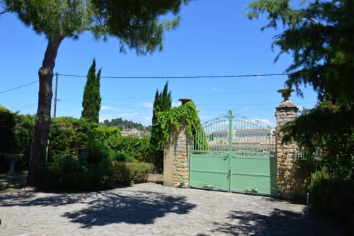 Grünes Eingangstor zur Villa Thébaïde B&B in Laudun L'Ardoise, Frankreich, mit Steinpfeilern und Zypressenbäumen