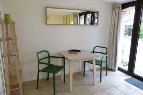 Bright dining area at Villa Thébaïde with wooden table, green chairs, mirror, and garden view patio access