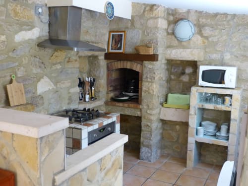 Rustic stone kitchen in Villa Thébaïde cottage with fireplace, stove, and modern appliances in Laudun L'Ardoise
