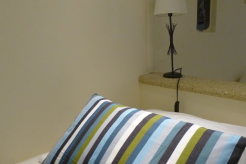 Striped pillow on bed in Cérise room at Villa Thébaïde with bedside lamp and garden view