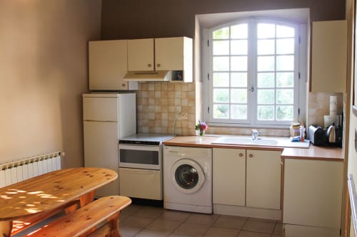 Bright cottage kitchen at Domaine de Lamartine with cream cabinets, washing machine, wooden dining table, and garden views
