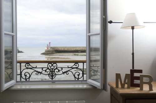 Open raam met zeezicht op de haven van Port-en-Bessin en MER-bord in een kamer van een Frans kusthuisje