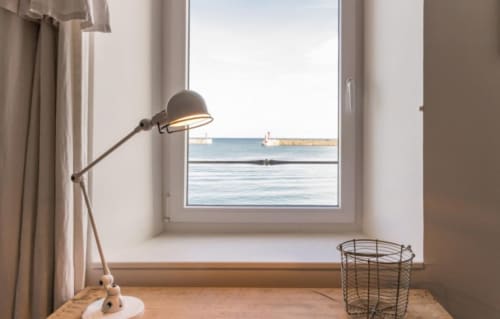 Espace de travail cottage côtier avec lampe de bureau ajustable surplombant le port de Port-en-Bessin et vue sur mer