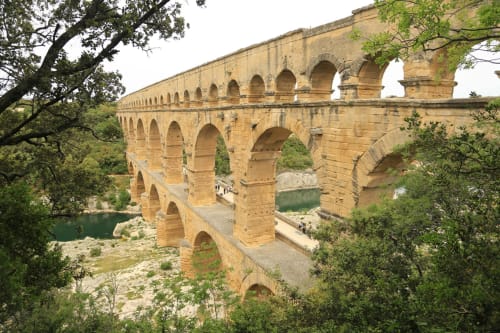 Ancient Roman aqueduct with three-tiered arches spanning green valley near Pont-Saint-Esprit, France