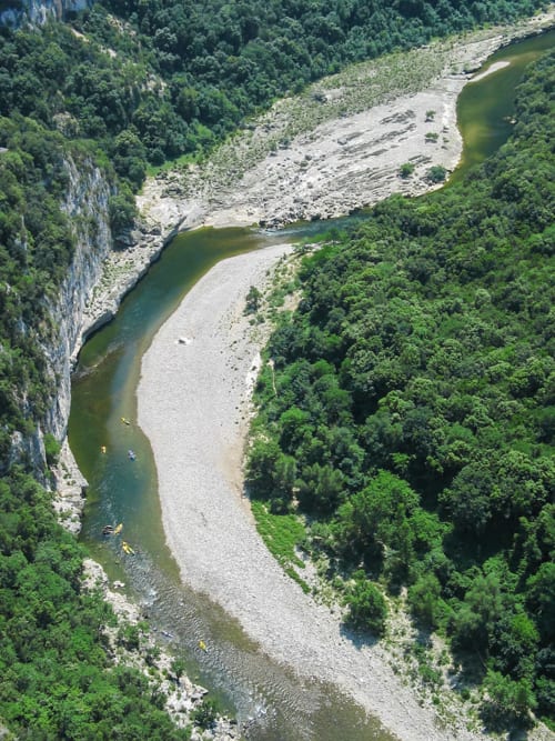 Aerial view of meandering river with kayakers surrounded by green forest and limestone cliffs near Pont-Saint-Esprit