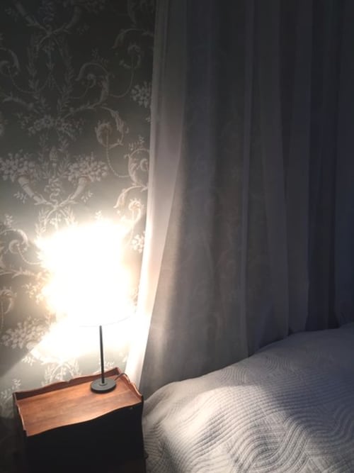 Bright bedroom at Domaine de Lamartine with patterned wallpaper, bed, nightstand with candle, and natural light from window