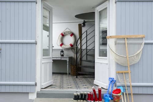 Charming beachside cottage entrance at Les Filles du Bord de Mer with nautical décor, life preserver, and fishing nets