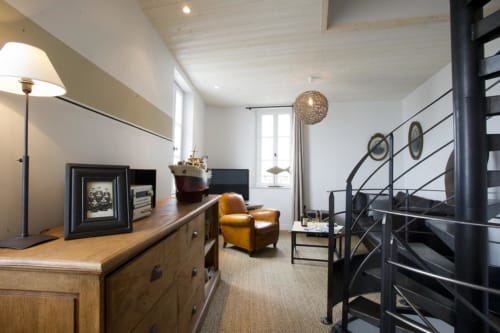Modern loft space at Les Filles du Bord de Mer with wooden furniture, tan armchair, and spiral staircase