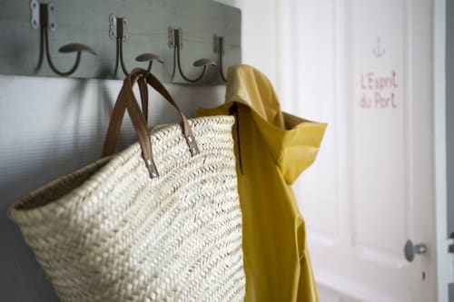 Panier tressé en paille avec anses marron et foulard jaune accrochés aux crochets métalliques de l'hôtel Les Filles du Bord de Mer