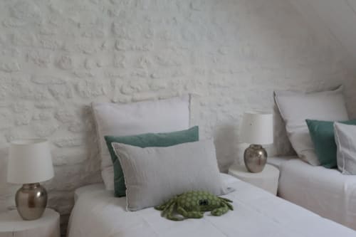Chambre côtière aux Filles du Bord de Mer avec murs en briques blanches, coussins verts et blancs, lampes en bronze et peluche