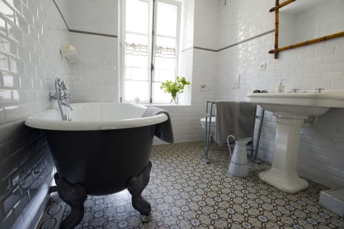 Elegant bathroom at Les Filles du Bord de Mer with black clawfoot tub, pedestal sink, and patterned tile floor in