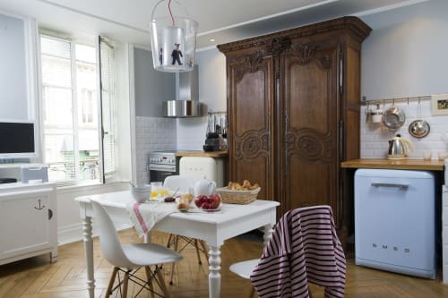 Charming vintage kitchen with Smeg refrigerator, ornate wooden armoire, and white dining table at Les Filles du Bord de Mer,