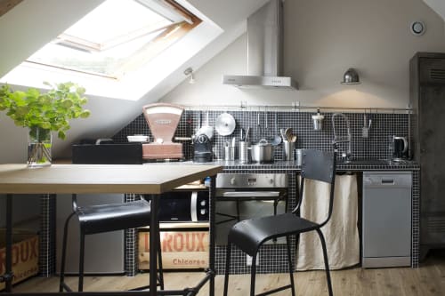 Modern attic kitchen in Port-en-Bessin with black tile backsplash, skylight, stainless appliances, and breakfast bar seating.
