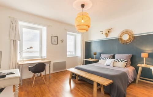 Modern bedroom at Les Filles du Bord de Mer with teal accent wall, wooden furniture, pendant light, and desk area in