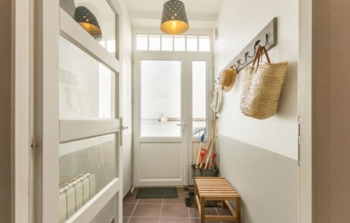 Bright entryway at Les Filles du Bord de Mer with pendant lights, storage hooks, wooden bench, and door to balcony