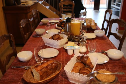 Mesa de desayuno en la Maison Addama B&B en Neyron con cruasanes, pan, jugo y cubiertos