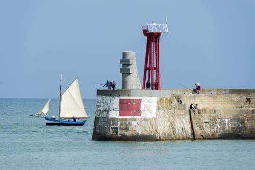 Voilier près du phare rouge du port en Bessin, France