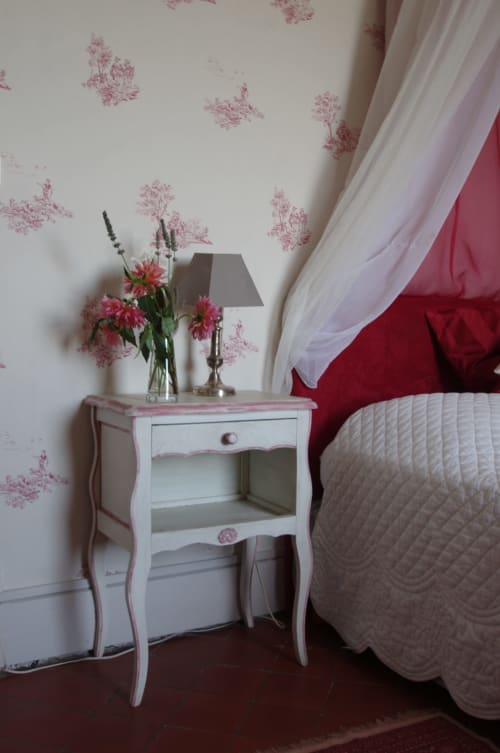 Elegant bedroom at Domaine de Lamartine with pink floral wallpaper, white nightstand, fresh flowers, and red bedding
