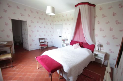 Elegant bedroom at Domaine de Lamartine with pink floral wallpaper, canopy bed, terracotta floor, and red velvet accents
