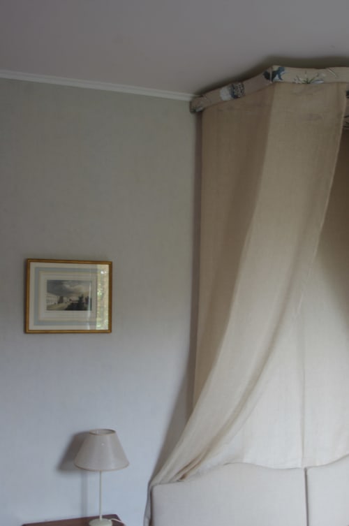 Bright bedroom at Domaine de Lamartine with cream curtains, framed landscape art, and bedside lamp in Pont-Saint-Esprit