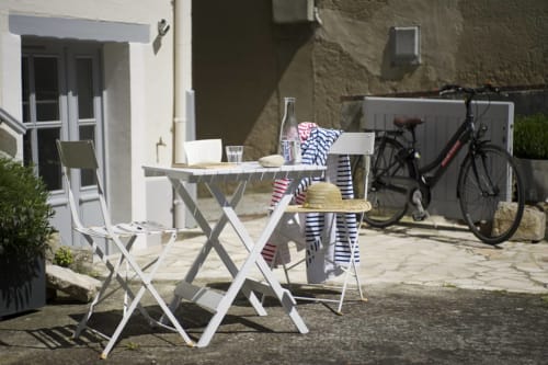 Zonnig binnenplein van cottage Les Filles du Bord de Mer met witte tuinmeubelen, fietsen en zeezicht in Port-en-Bessin