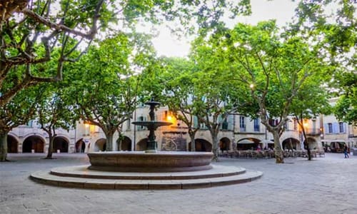 Charmante place de Laudun L'Ardoise avec fontaine, bâtiments à arcades et arbres centenaires