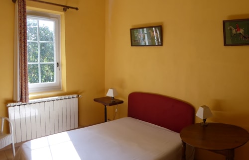 Bright yellow bedroom at Domaine de Lamartine cottage with red headboard bed, white radiator, and garden views through window