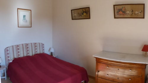 Cozy cottage bedroom at Domaine de Lamartine with burgundy bedding, patterned headboard, wooden dresser, and framed artwork