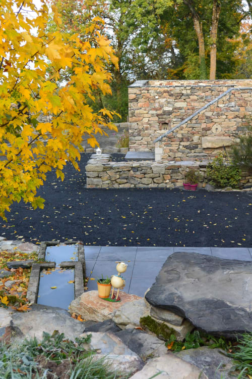 Jardin d'automne aux Pays Des Sucs avec feuillages dorés, murs en pierre, étang miroir et décors automnaux à Saint-Hostien