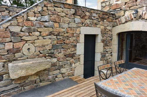 Terrasse en pierre avec murs rustiques, porte noire, chaises en bois et carrelage en terre cuite au gîte Aux Pays Des Sucs