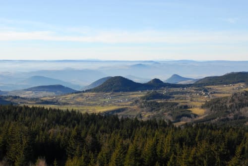 Vue panoramique de la vallée avec collines boisées, villages dispersés et montagnes près du Gîte Aux Pays Des Sucs à Saint-Hostien