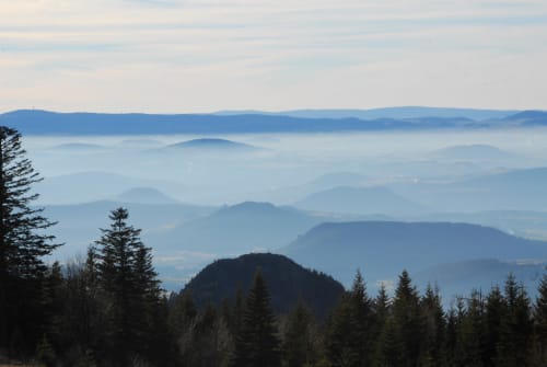 Vue des couches de montagnes brumeuses depuis Aux Pays Des Sucs à Saint-Hostien, France, avec forêt de conifères