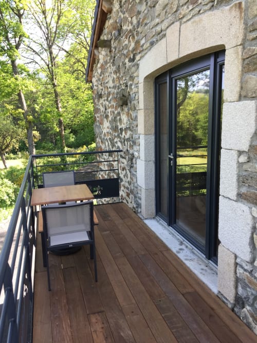 Terrasse moderne en bois avec chaise à Aux Pays Des Sucs B&B à Saint-Hostien, bâtiment en pierre avec portes-fenêtres noires
