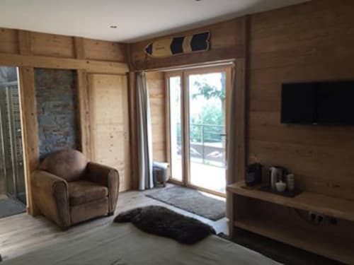 Intérieur moderne de chalet en bois aux Pays Des Sucs avec fauteuil, télévision et portes vitrées ouvrant sur balcon, Saint-Hostien