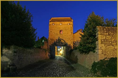Tour-porche en pierre illuminée du Domaine de La Serita à Joze, France, au crépuscule avec murs couverts de lierre.