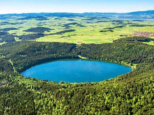 Vue aérienne d'un lac bleu cristallin entouré de forêt dense près d'Aux Pays Des Sucs à Saint-Hostien, France