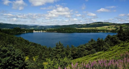 Lac bleu entouré de forêts vertes et collines ondulantes près du gîte Aux Pays Des Sucs à Saint-Hostien, France