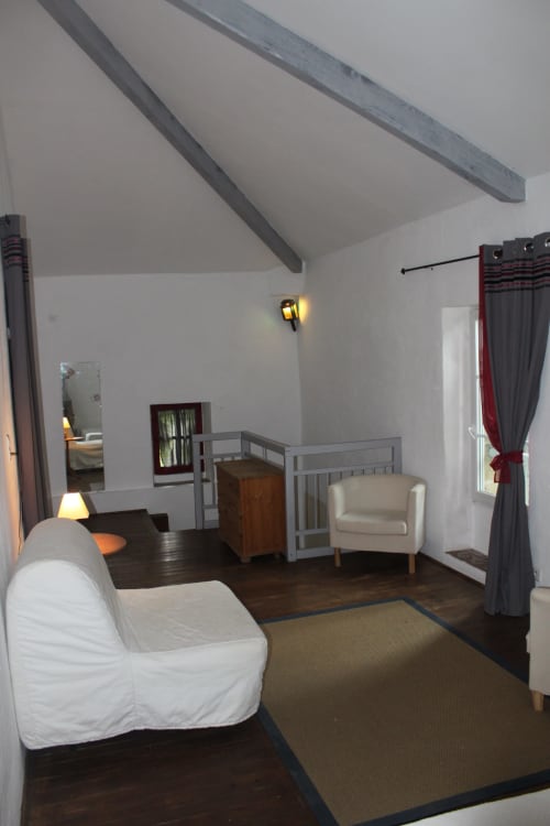 Ramona cottage bedroom at Domaine de Lamartine with white sofa, crib, beamed ceiling, and garden view in Pont-Saint-Esprit