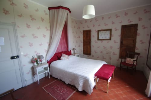 Elegant bedroom at Domaine de Lamartine with four-poster bed, red damask wallpaper, and traditional French decor in