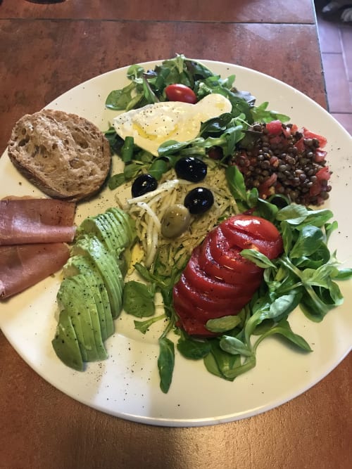 Gourmet brunch plate at Le Pignié B&B featuring avocado, poached egg, lentil salad, red pepper, prosciutto, and fresh greens