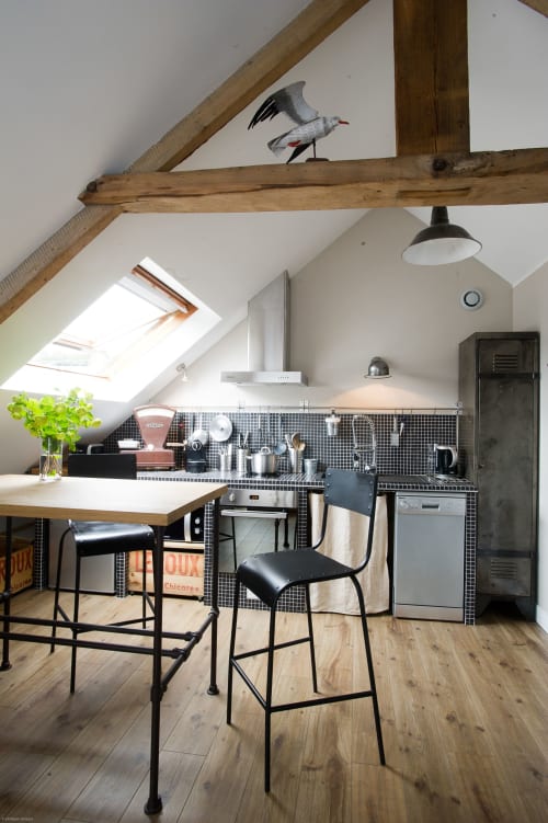 Moderne Loft-Küche mit freiliegenden Balken, schwarzem Fliesenspritzschutz, Holztheke mit schwarzen Hockern und Vogelkunst im Les