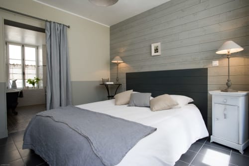 Chambre moderne aux Filles du Bord de Mer à Port-en-Bessin avec tête de lit noire, literie blanche et mur en lambris.