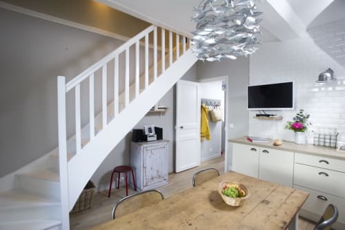Cuisine-salle à manger moderne de l'appartement L'Esprit du port à Port-en-Bessin avec table en bois, placards blancs et escalier.