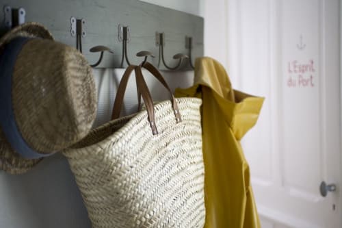 Panier tissé et vêtement jaune accrochés aux crochets de l'appartement Les Filles du Bord de Mer, Port-en-Bessin