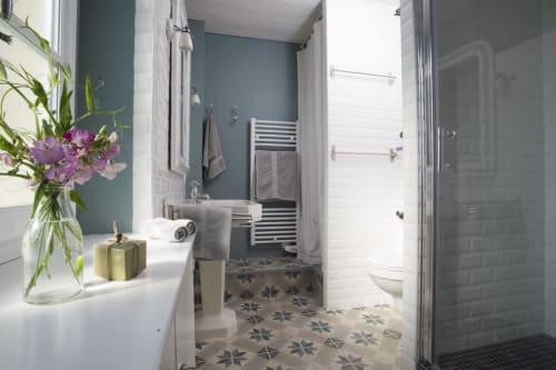 Salle de bains moderne aux murs bleu-vert, carrelage à motifs, douche, toilettes et fleurs violettes fraîches aux Filles du Bord de Mer