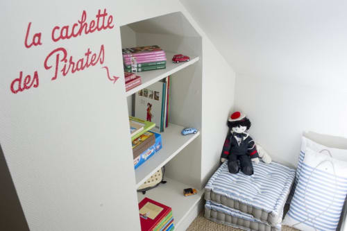 Chambre d'enfant thématique pirate avec étagères blanches, literie rayée et texte mural "la cachette des Pirates" aux Filles