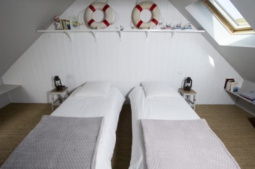Lits jumeaux dans la chambre mansardée au style nautique des Filles du Bord de Mer, Port-en-Bessin avec bouées de sauvetage et vue sur le port